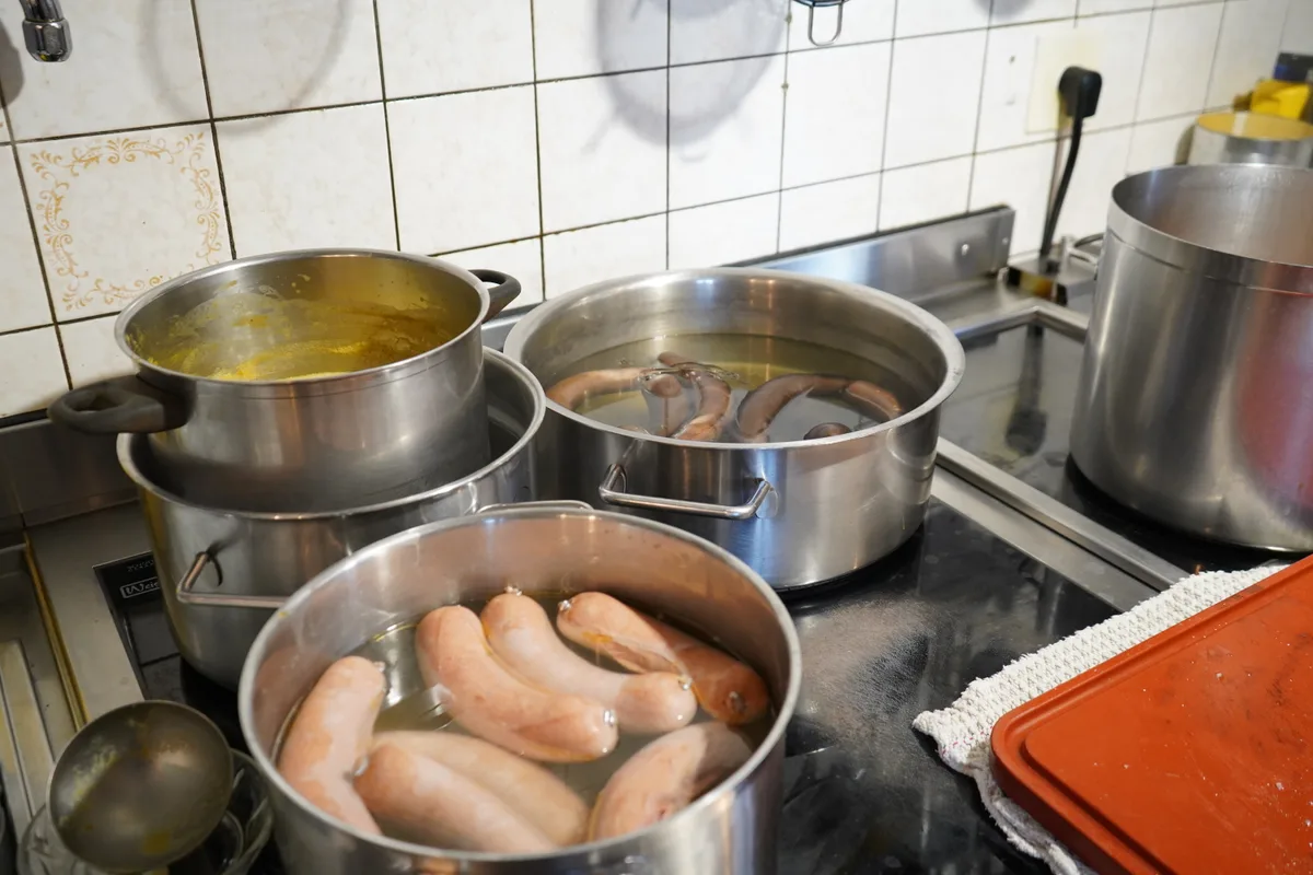 Würste liegen in Kochtöpfen im Wasser.